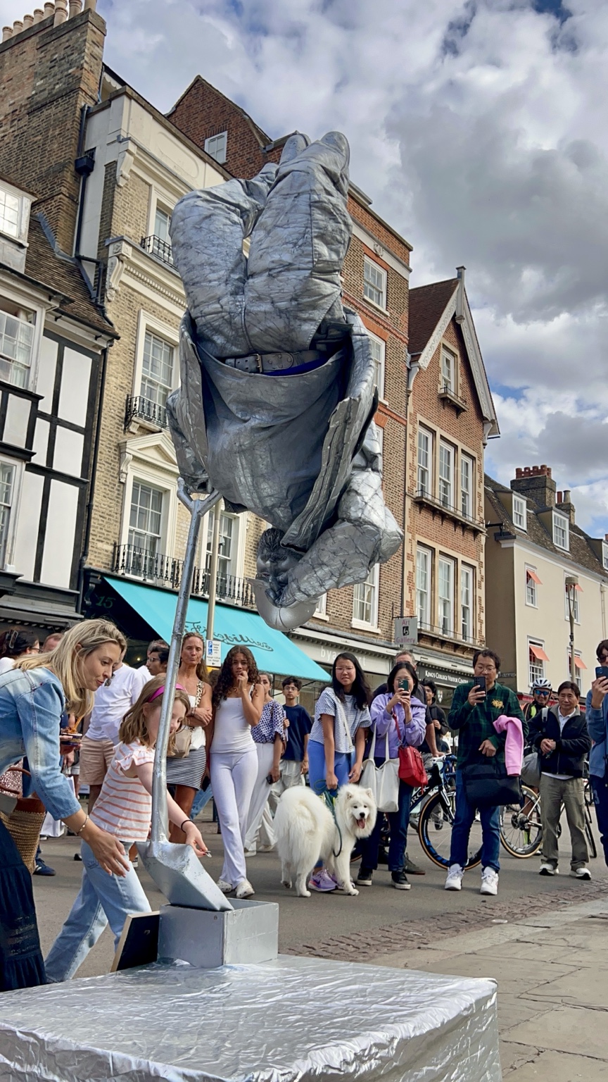 Silverman Statue Builder performing upside down with his signature shovel before a street audience